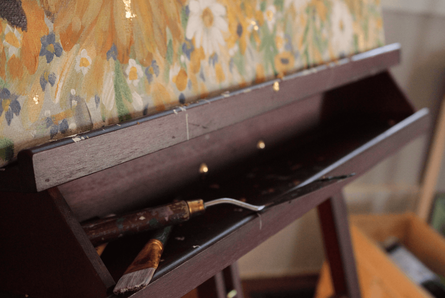 Close-up of a wooden drawer with floral fabric on top, containing a paintbrush and other items.