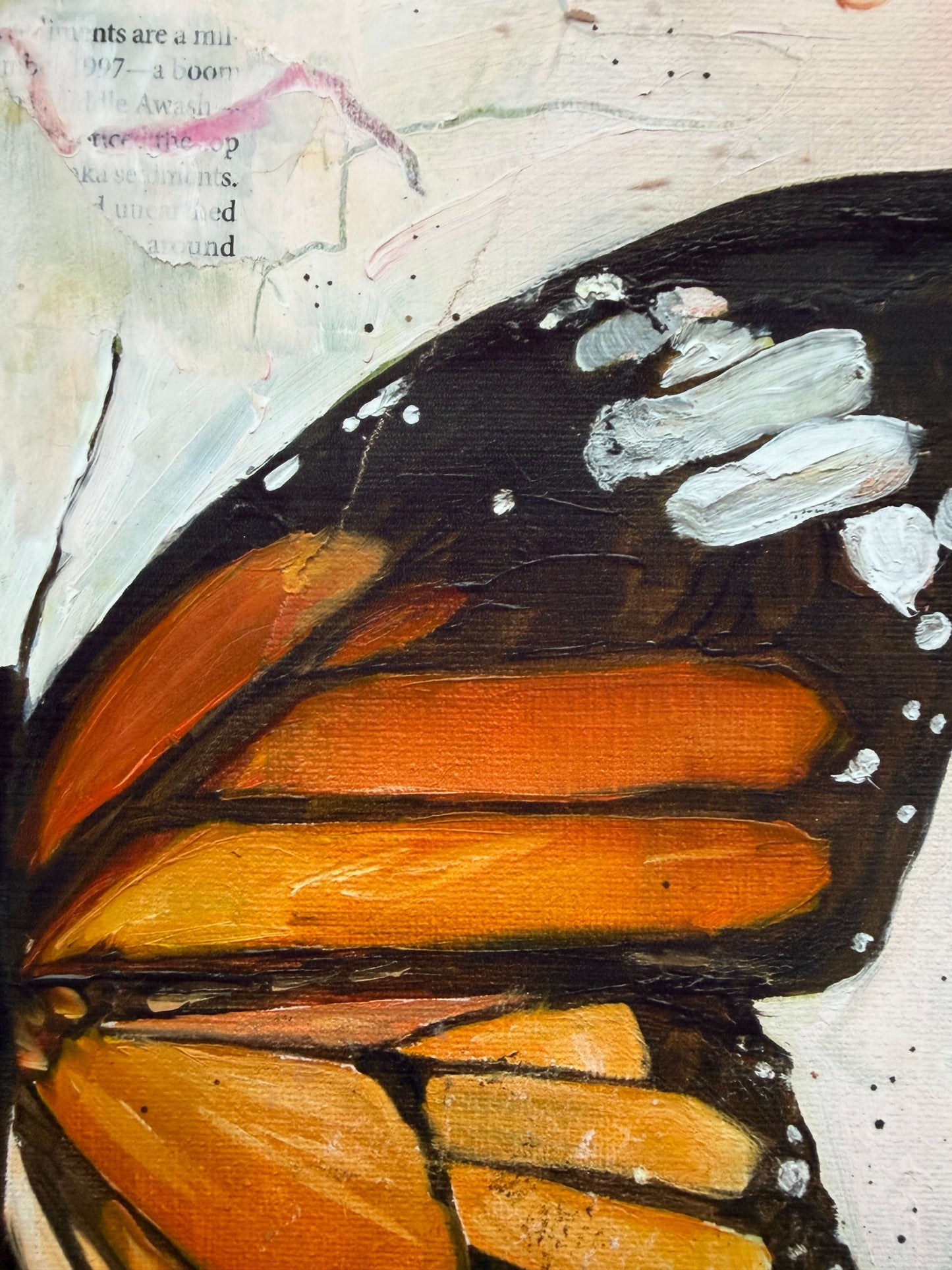 Close-up of a painted butterfly wing with orange and black bands on a textured off-white background with faint text and paint splatters.