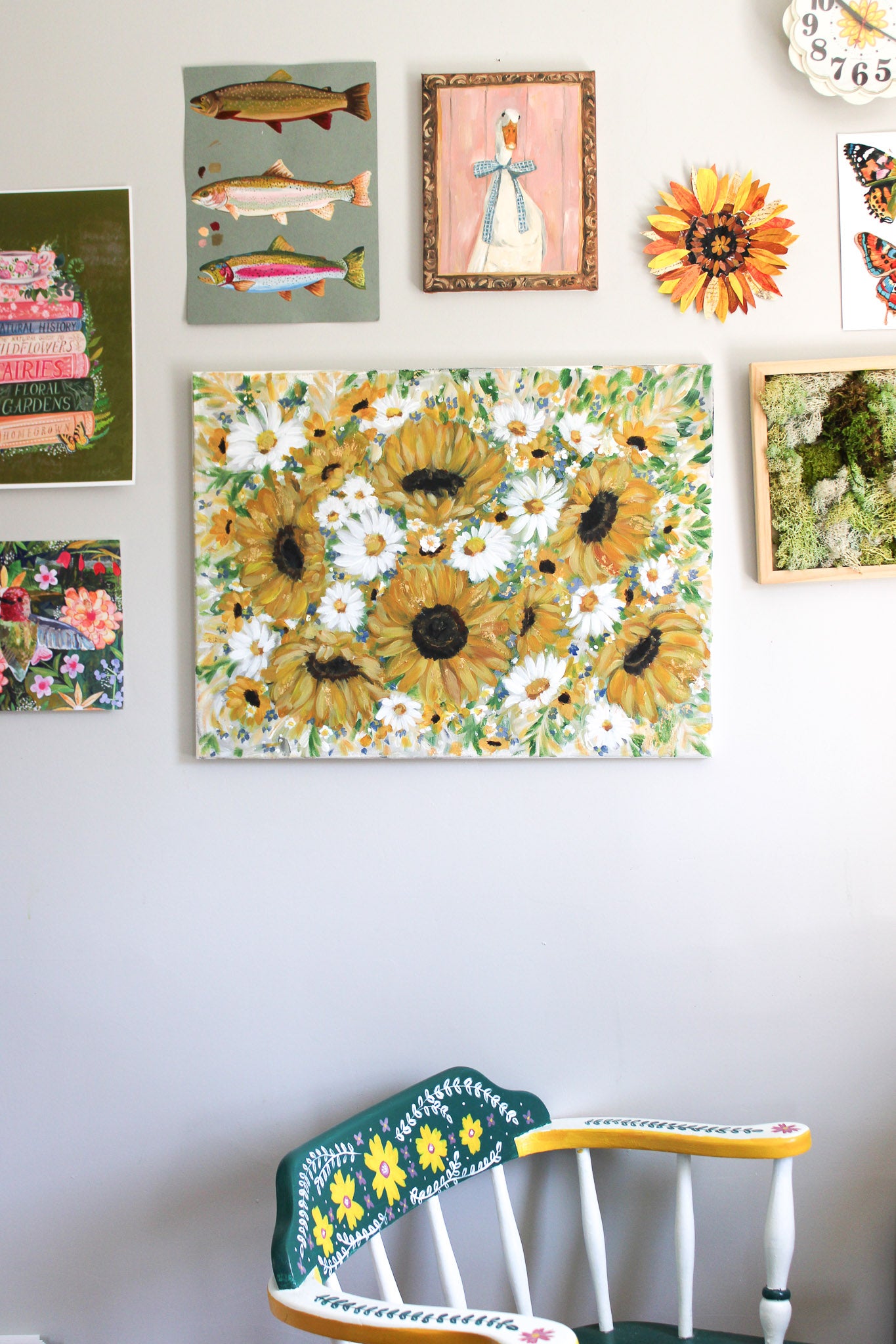 Wall with various framed artworks including a prominent sunflower painting, colorful chair below, and decorative elements.