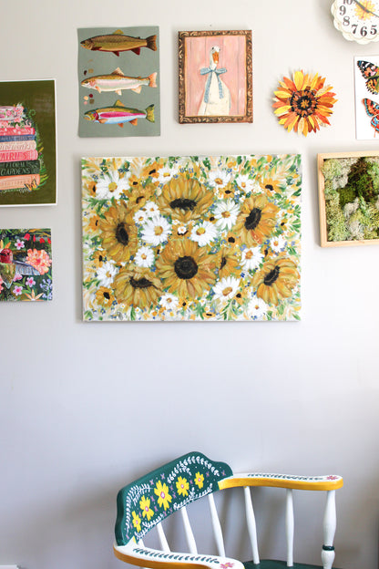 Wall with various framed artworks including a prominent sunflower painting, colorful chair below, and decorative elements.