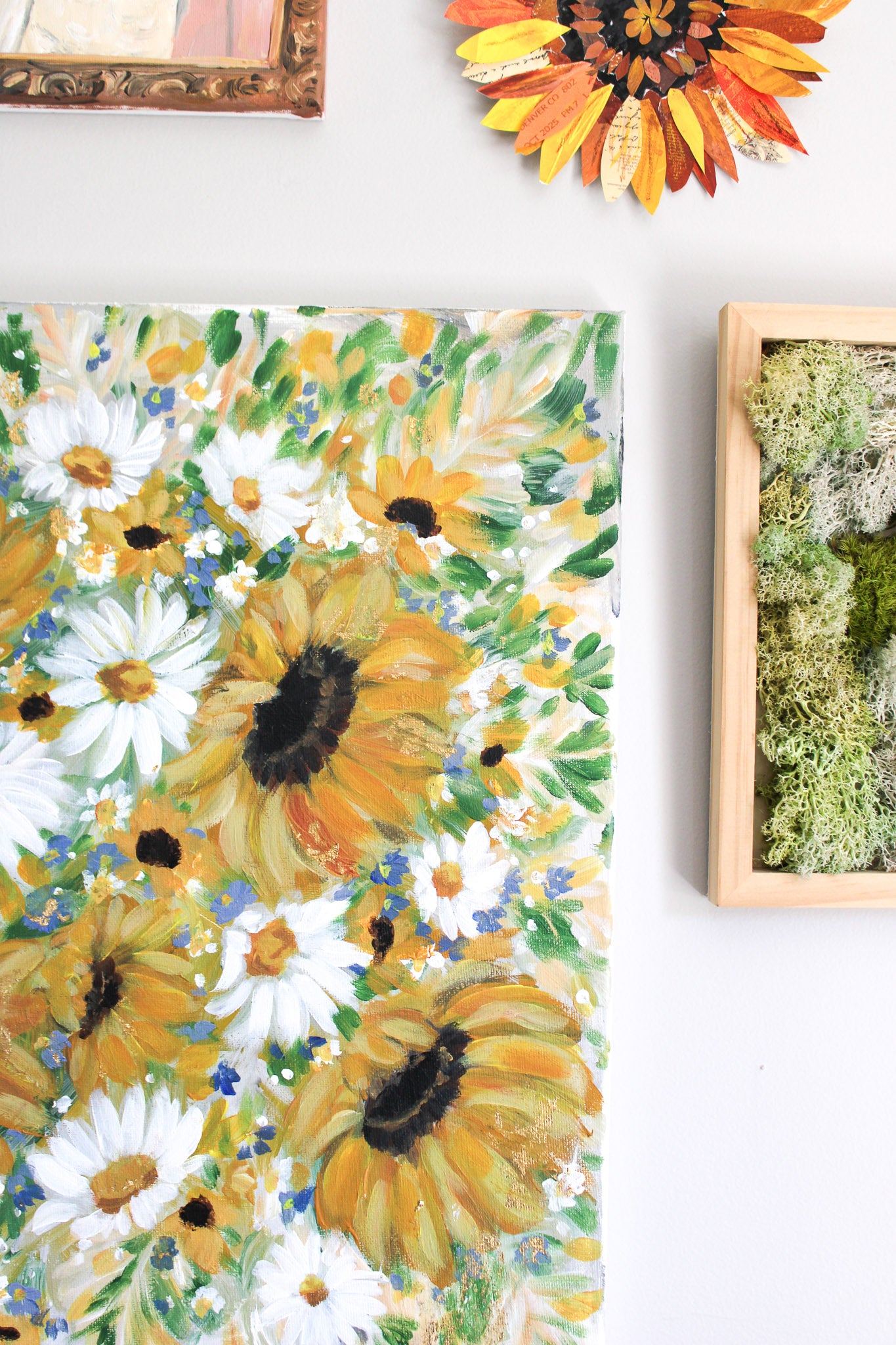 Floral painting with sunflowers and daisies on a white wall.