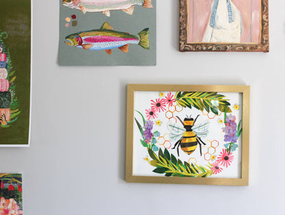 Framed artwork of a bee and flowers on a wall with other framed pictures.