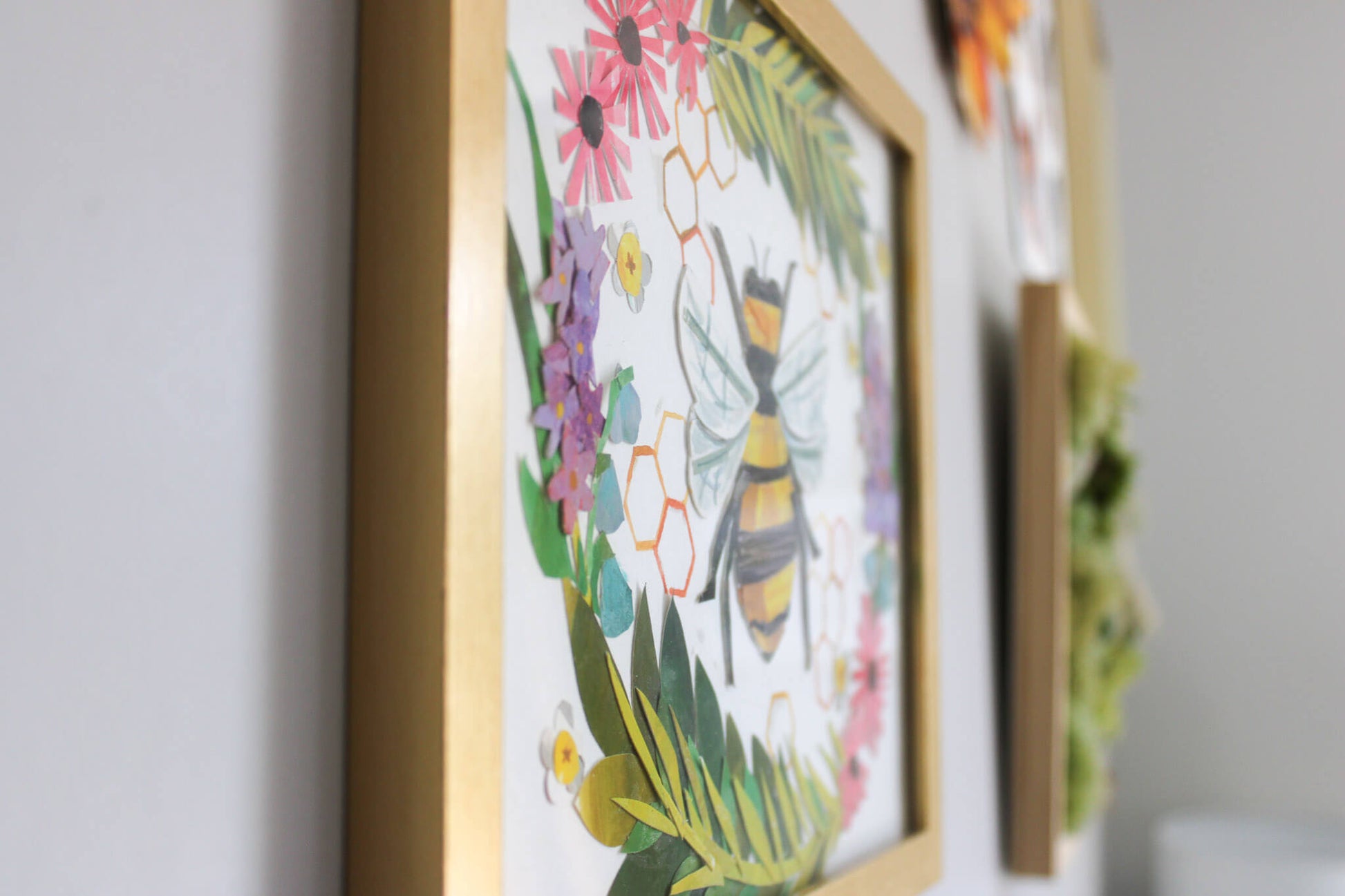 Framed artwork with a bee and floral design on a wall.
