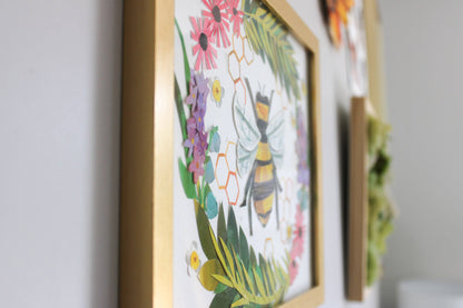Framed artwork with a bee and floral design on a wall.