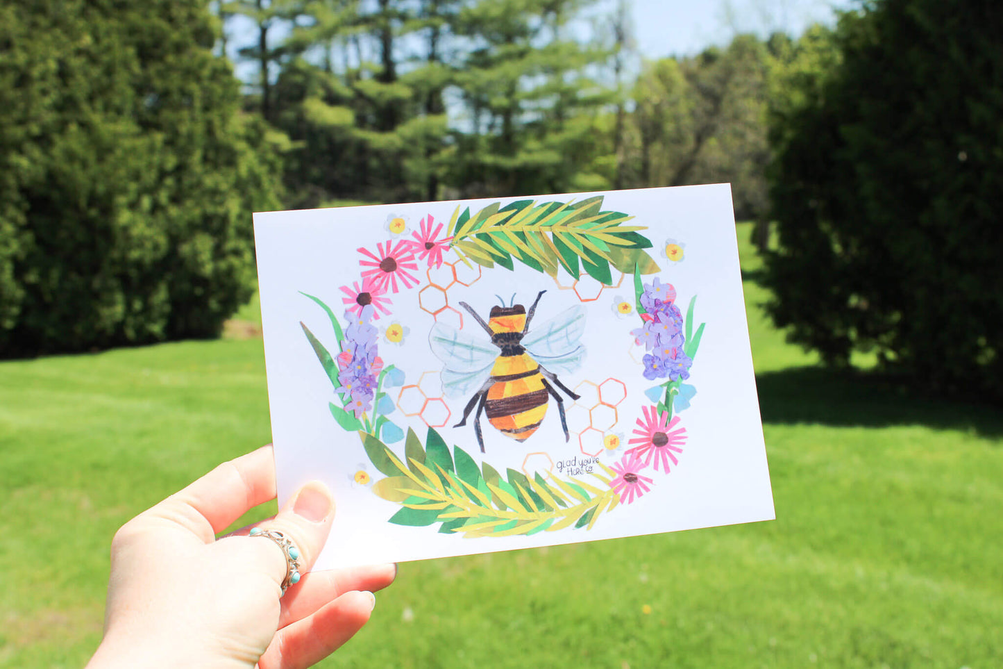 Hand holding an art print of a bee collge in a garden setting