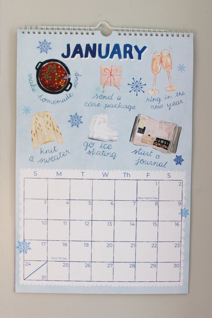 A January wall calendar with a light blue background, decorated with hand-drawn illustrations and prompts for holiday activities, shown hanging on a neutral wall.