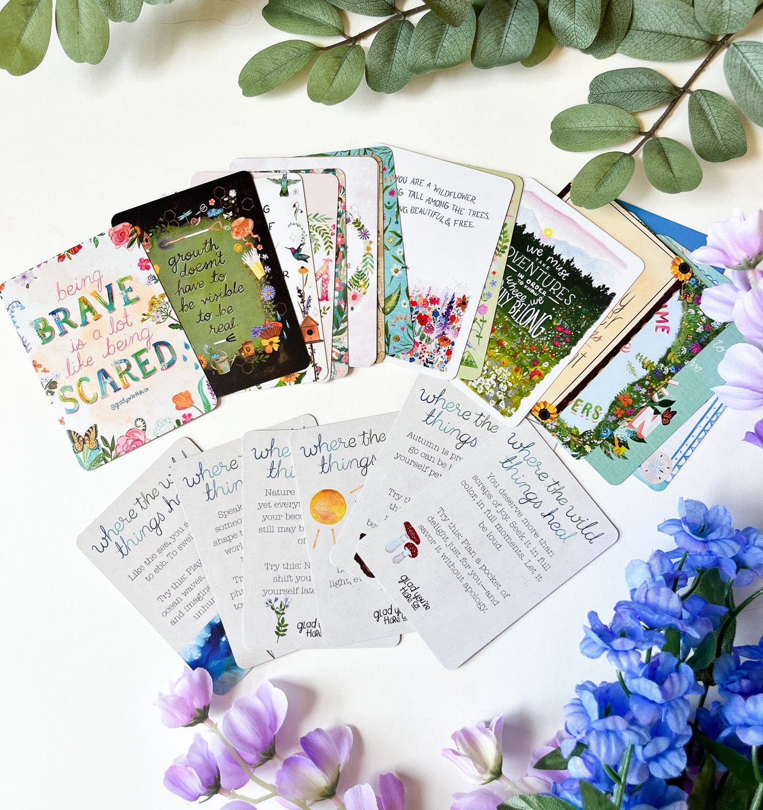 Collection of colorful cards with text and illustrations on a white surface with green and purple flowers.