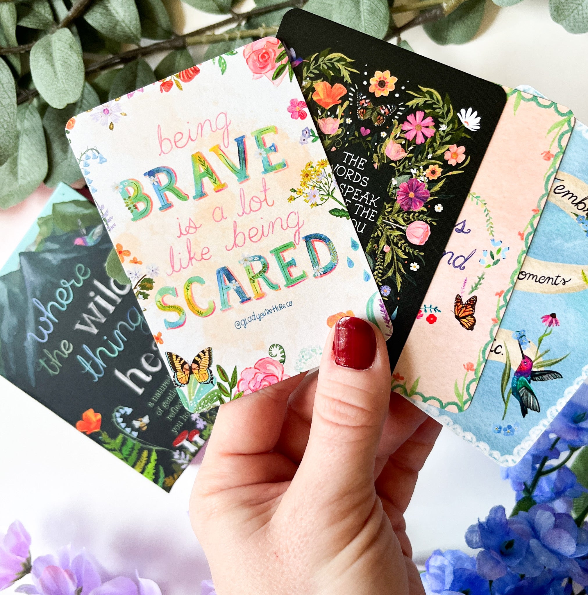 Hand holding a colorful card with motivational quote surrounded by flowers and leaves