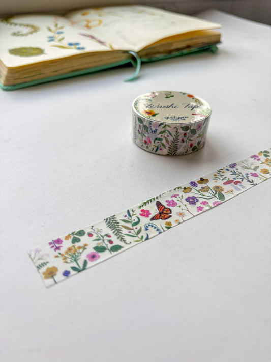 Roll of floral washi tape with a strip on a white surface, next to an open notebook.