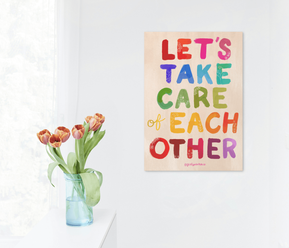 Poster with motivational quote 'Let's take care of each other' on a white wall with a vase of tulips.