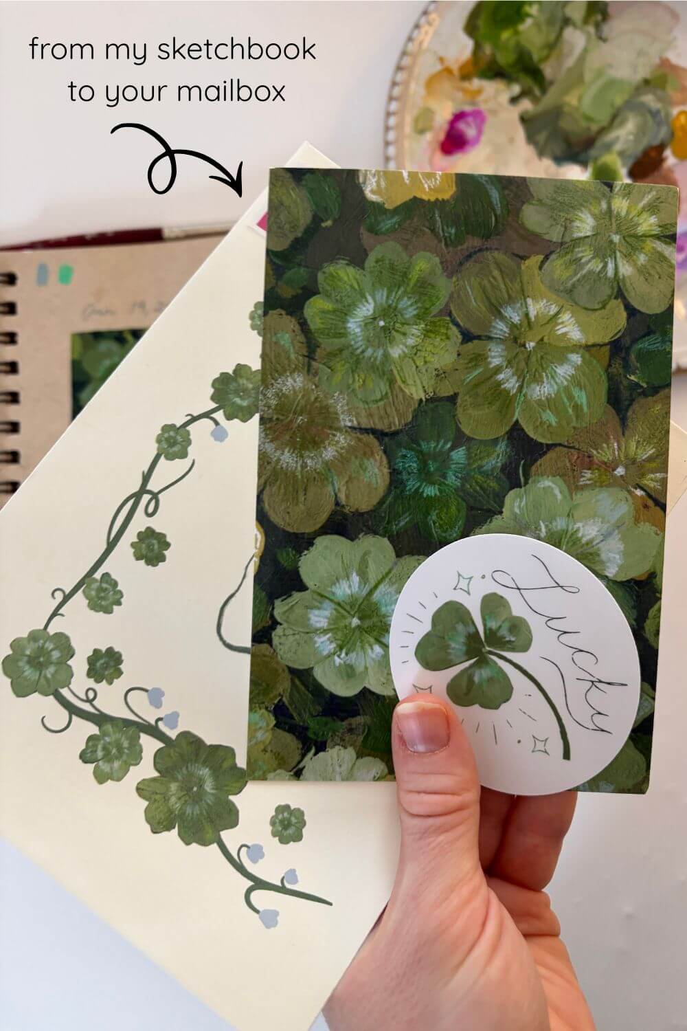 Hand holding a card with green floral design and 'Lucky' sticker, with text 'from my sketchbook to your mailbox'.