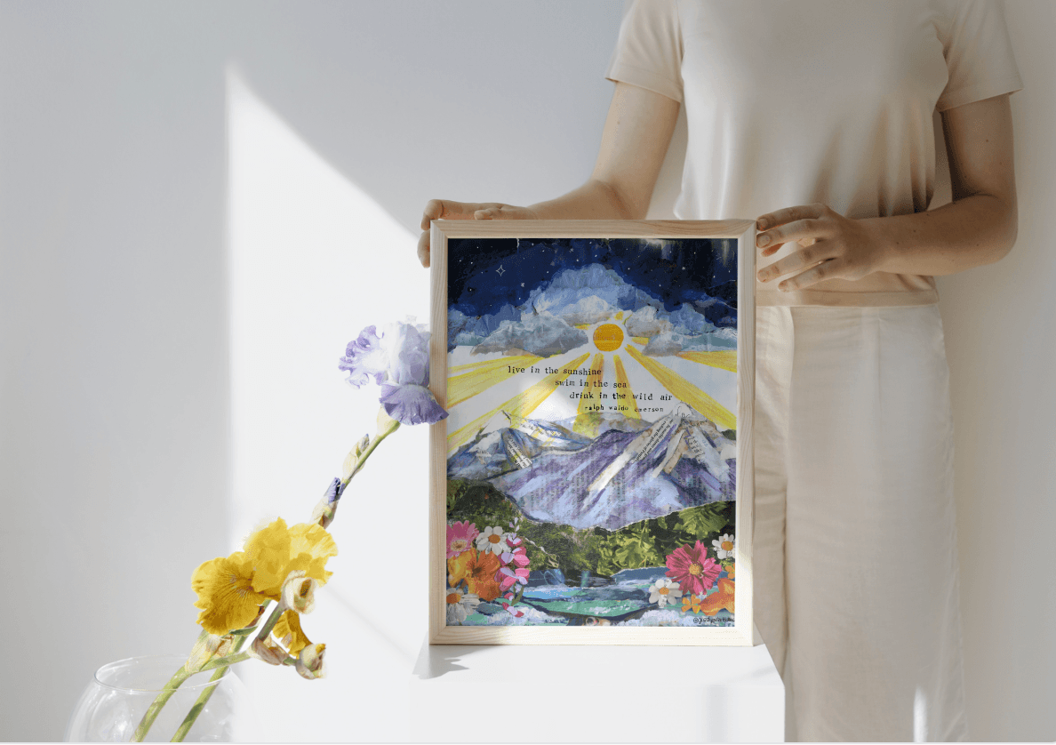 Person holding a framed artwork with mountains and flowers, surrounded by flowers on a light background