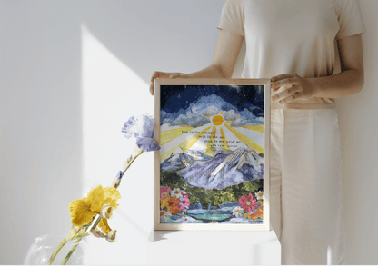 Person holding a framed artwork with mountains and flowers, surrounded by flowers on a light background