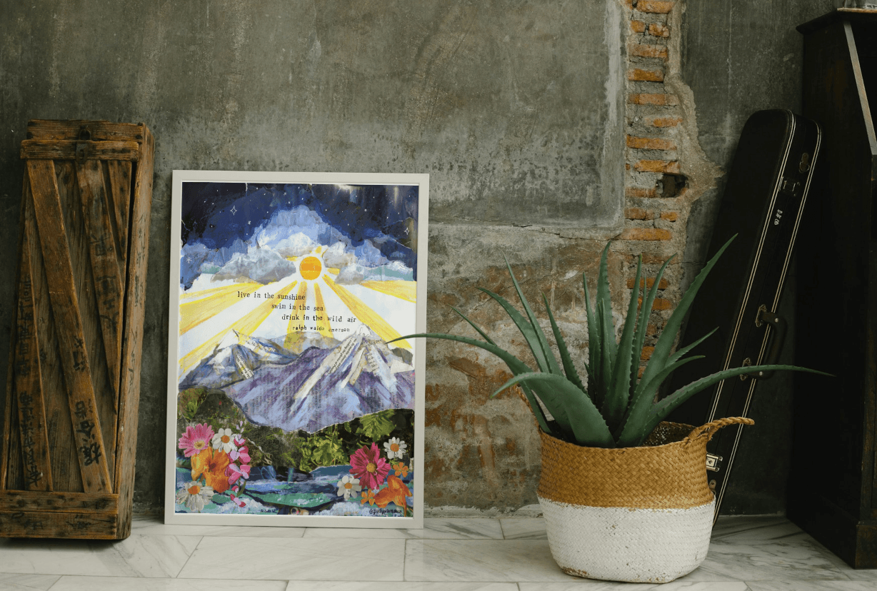 Framed artwork of a mountain landscape with flowers on a concrete wall, next to a potted plant.