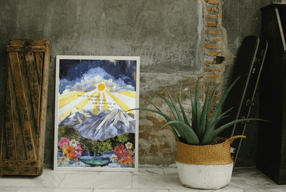 Framed artwork of a mountain landscape with flowers on a concrete wall, next to a potted plant.