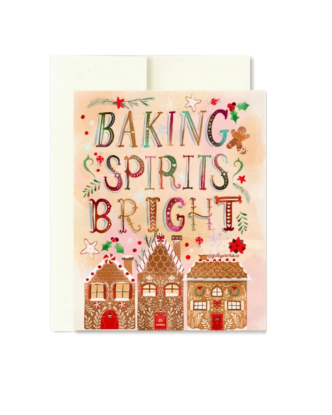 A Christmas baking-themed greeting card with the phrase 'BAKING SPIRITS BRIGHT' in decorative lettering above three gingerbread houses, shown with an off-white envelope behind it on a white background.
