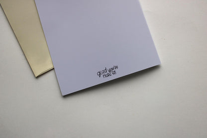Two greeting cards, one beige and one purple, on a light gray surface.