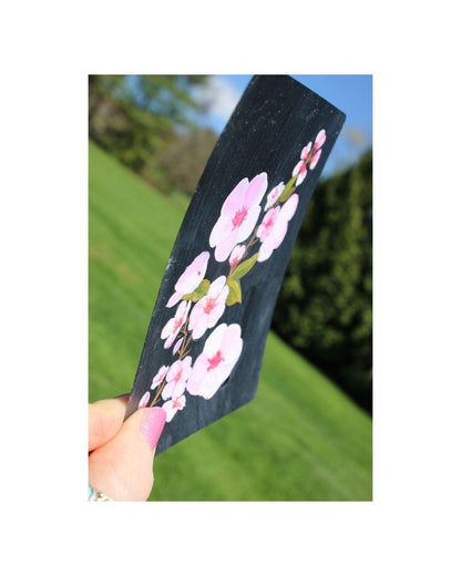 Hand holding a black notebook with pink floral design against a blurred green outdoor background