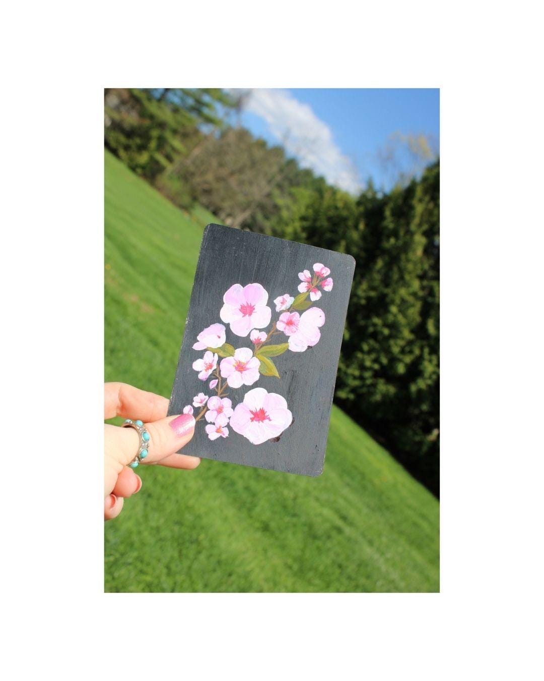 Hand holding a card with cherry blossom design against a natural background