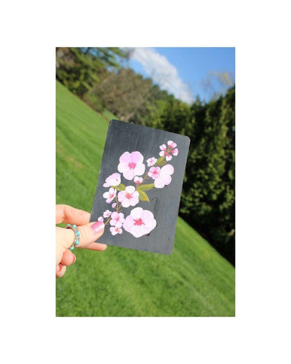 Hand holding a card with cherry blossom design against a natural background