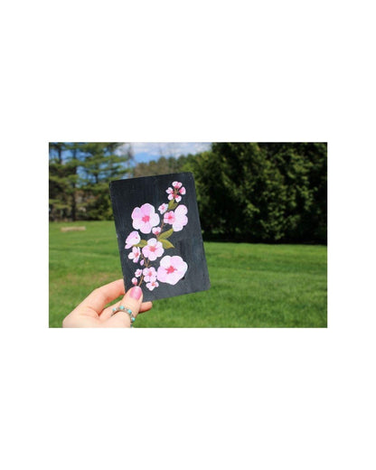 Hand holding a card with cherry blossom design against a natural background