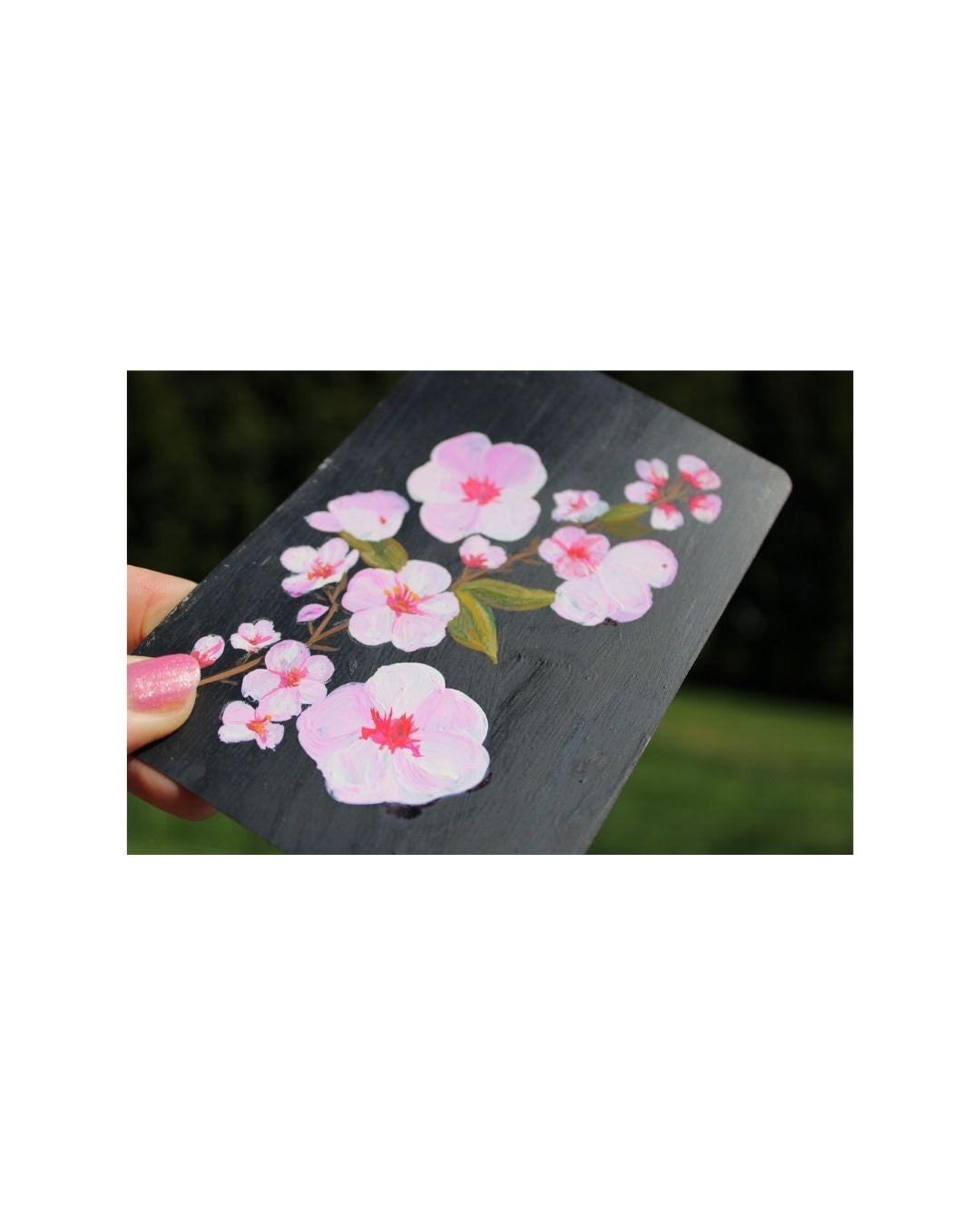 Card with pink floral design held by a hand against a blurred natural background