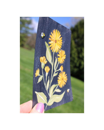 Decorative wooden sign with yellow flowers and a bee on a grassy background