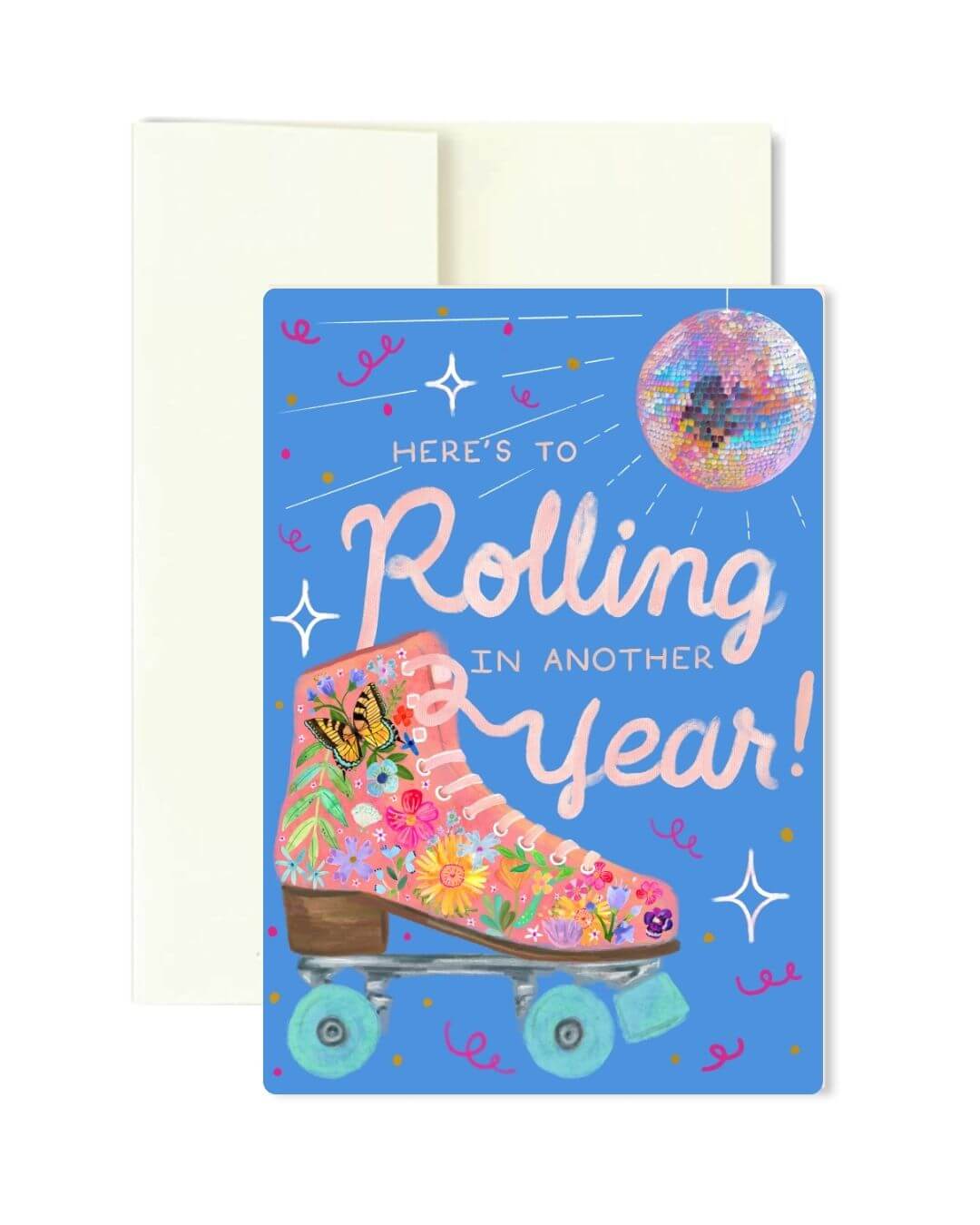 A blue greeting card with a floral roller skate illustration and the text 'Here's to Rolling in Another Year!' shown in front of a cream envelope on a white background.