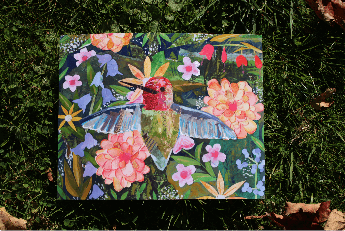 Colorful artwork of a hummingbird and flowers on grass