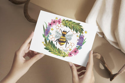 Person holding a card with a bee and floral design on a beige surface