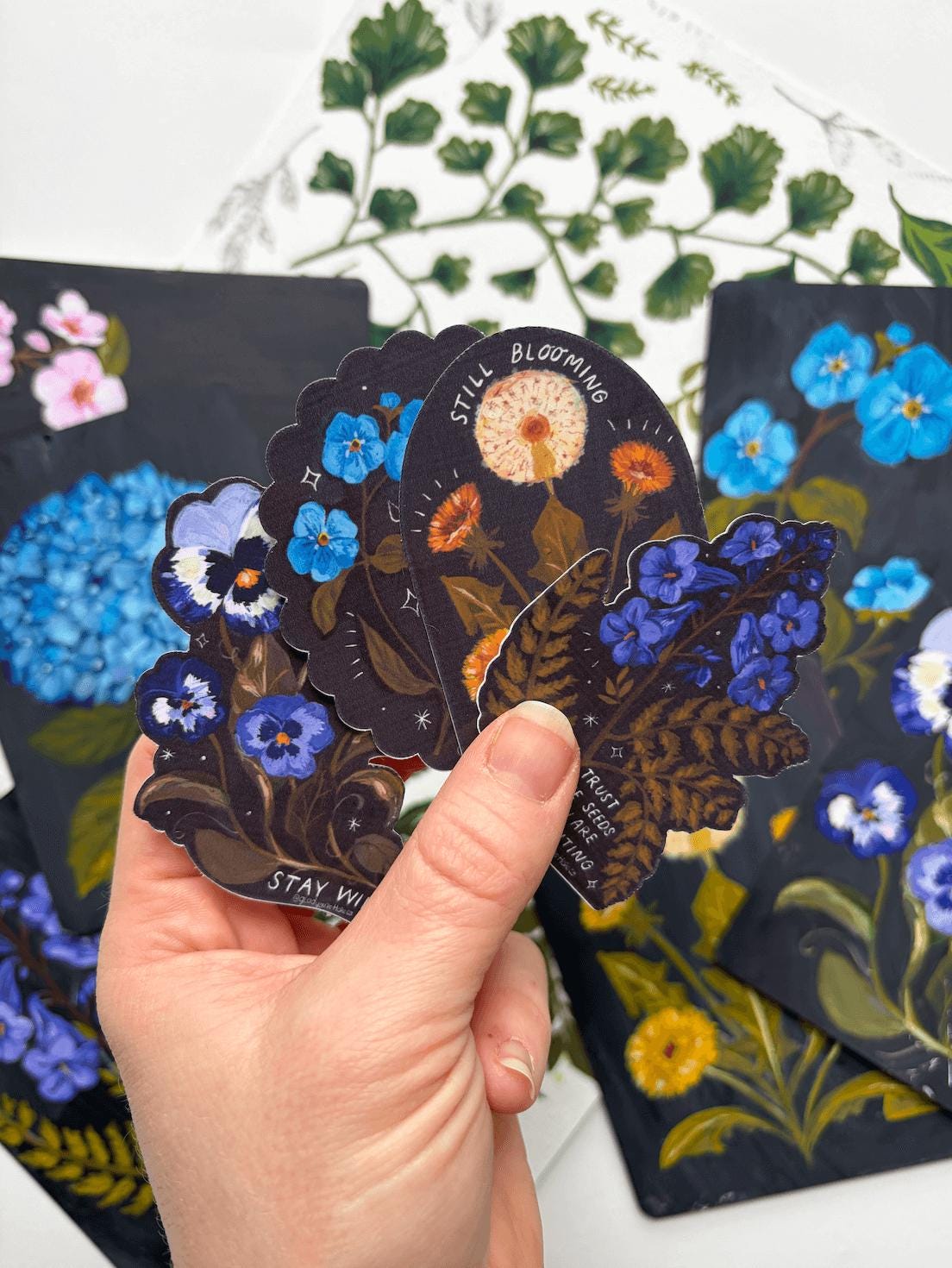 Hand holding a set of floral-themed cards with detailed illustrations on a white background.