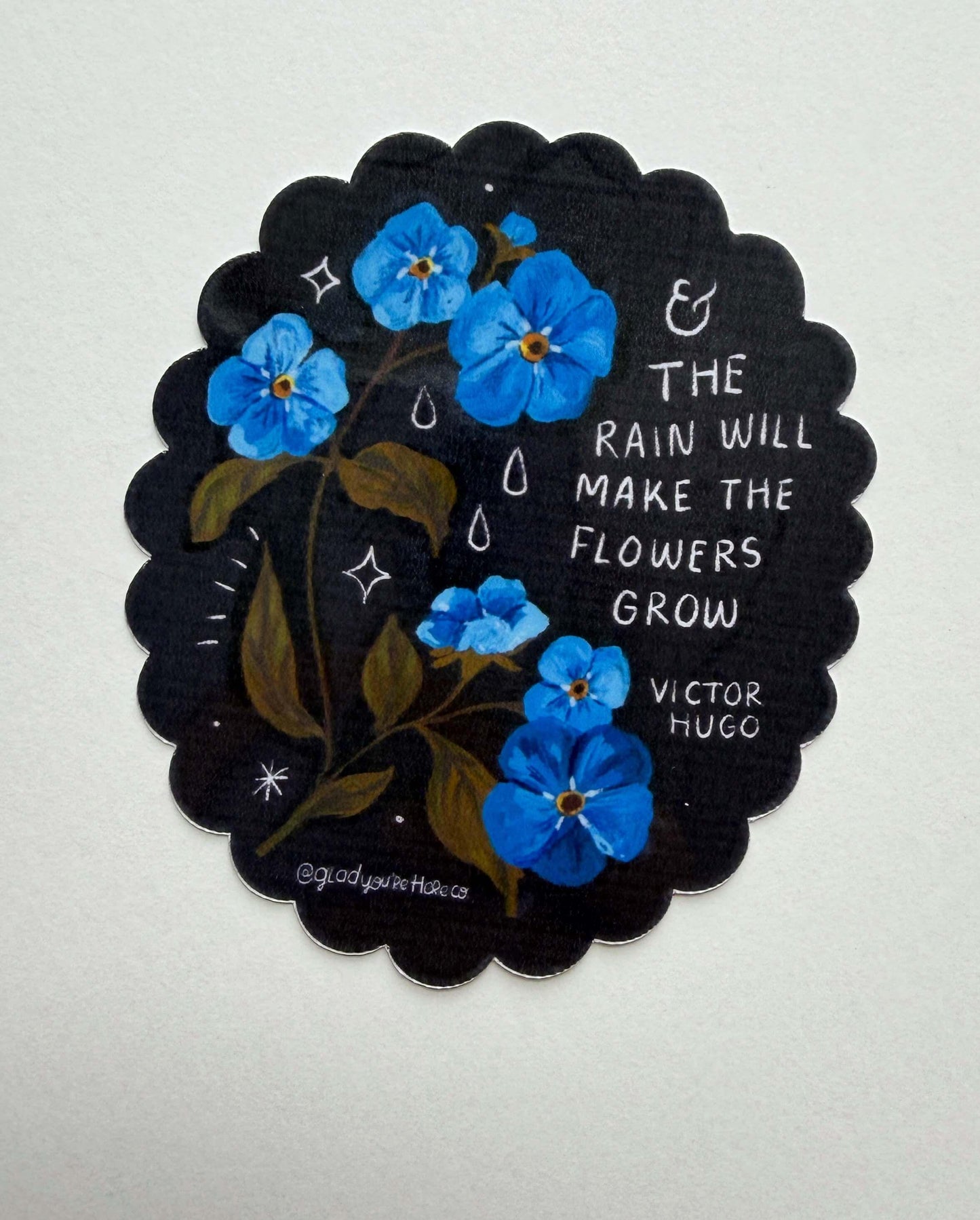 Decorative sticker with blue flowers and a quote by Victor Hugo on a black scalloped border.