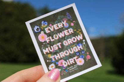 Sticker with motivational quote held by a hand against a blurred natural background