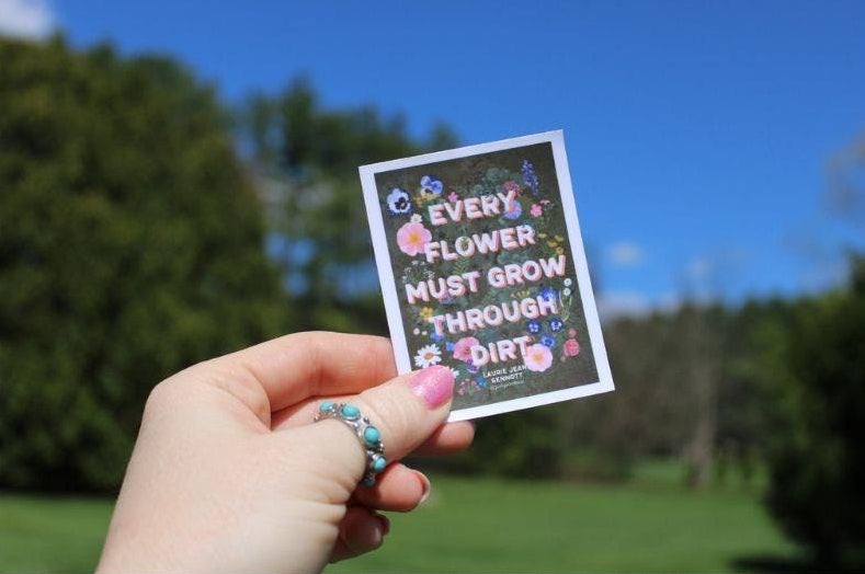 Hand holding a sticker with text and illustrations against a natural background