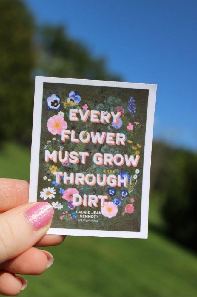 Sticker with floral design and motivational quote held against a natural background