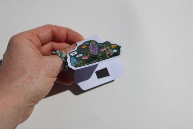 Hand holding a small wildfllower magnetic bookmark with a floral design on a white background
