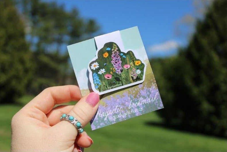 Hand holding a wildflower magnetic bookmark with a floral design outdoors
