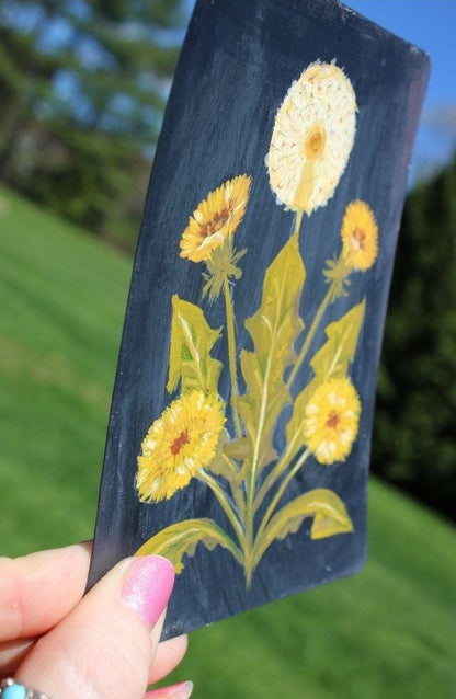 Hand holding a card with yellow floral design against a blurred natural background