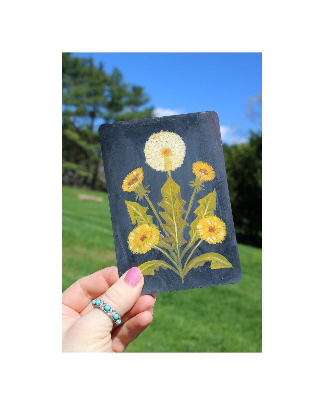 Hand holding a card with yellow floral design against a natural background