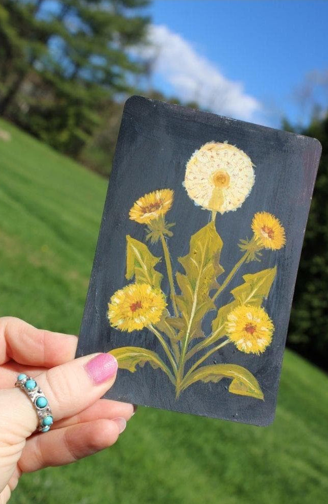 Hand holding a card with dandelion design against a natural background