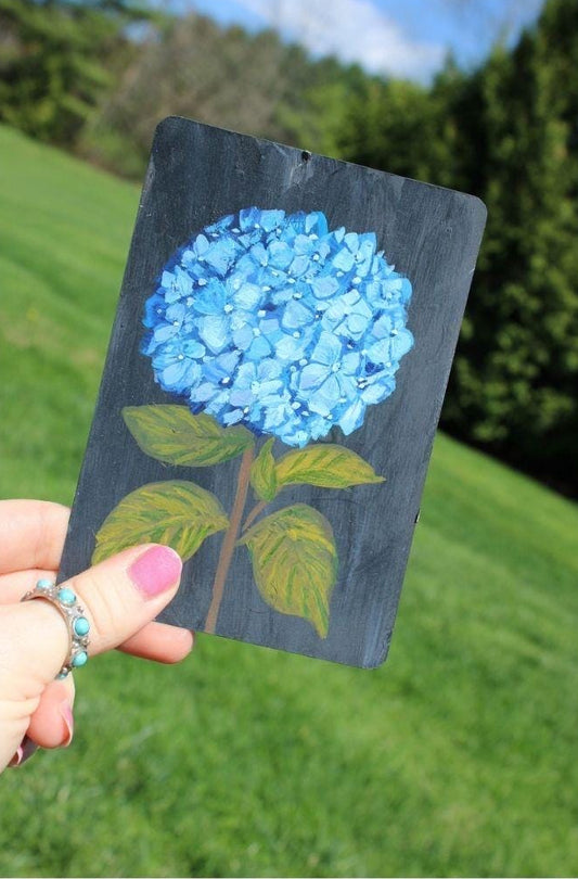 Hand holding a card with a blue flower design against a grassy background
