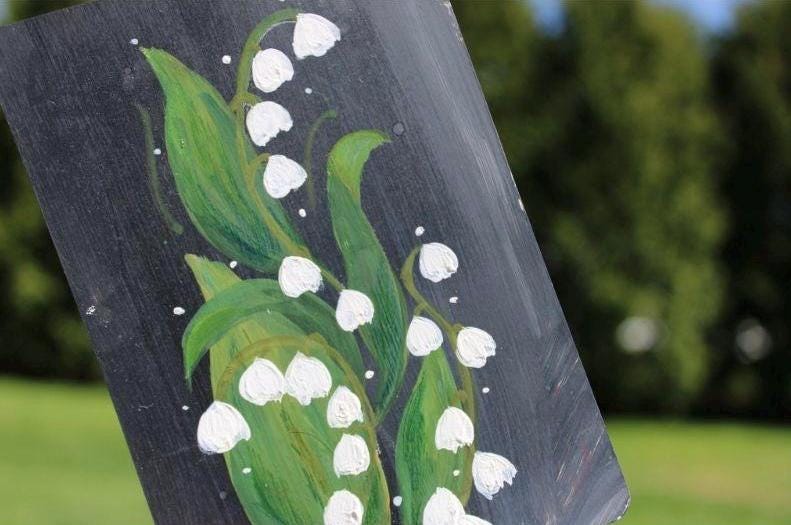 Painting of lilies of the valley on a dark background with green leaves and white flowers.