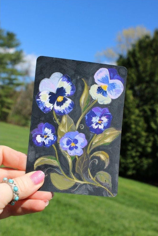 Hand holding a card with floral design against a natural background
