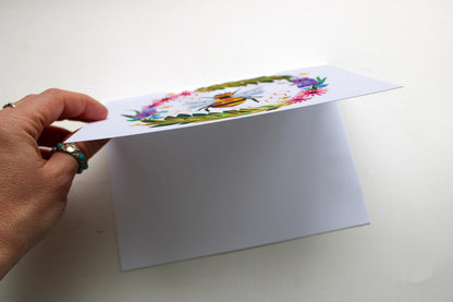 Hand holding a white card with floral design on a white background