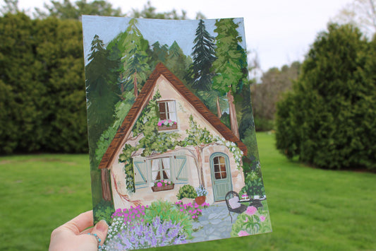 Hand holding a painting of a quaint house with greenery