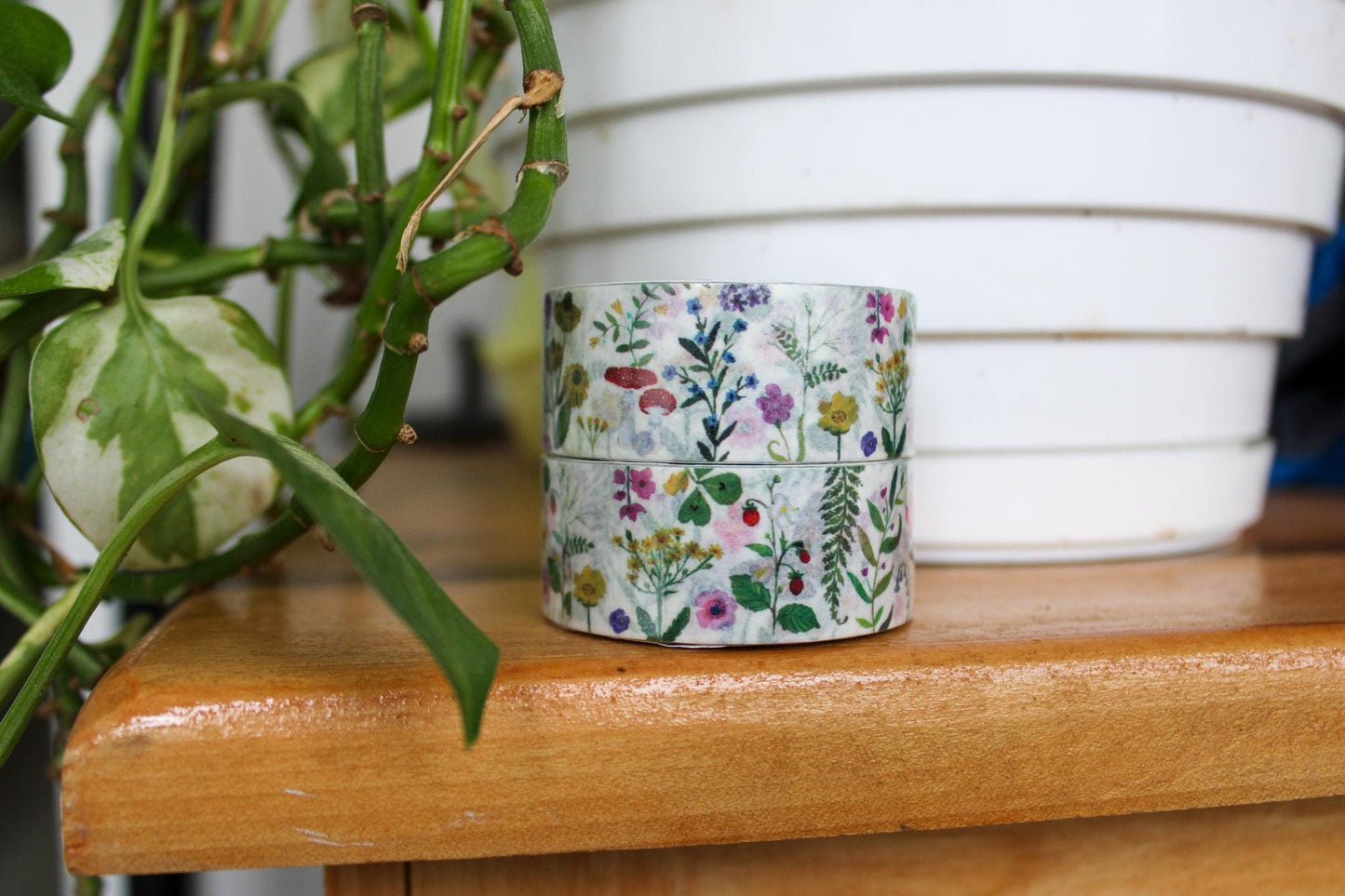 Stack of floral-patterned tape on a wooden surface with a plant in the background