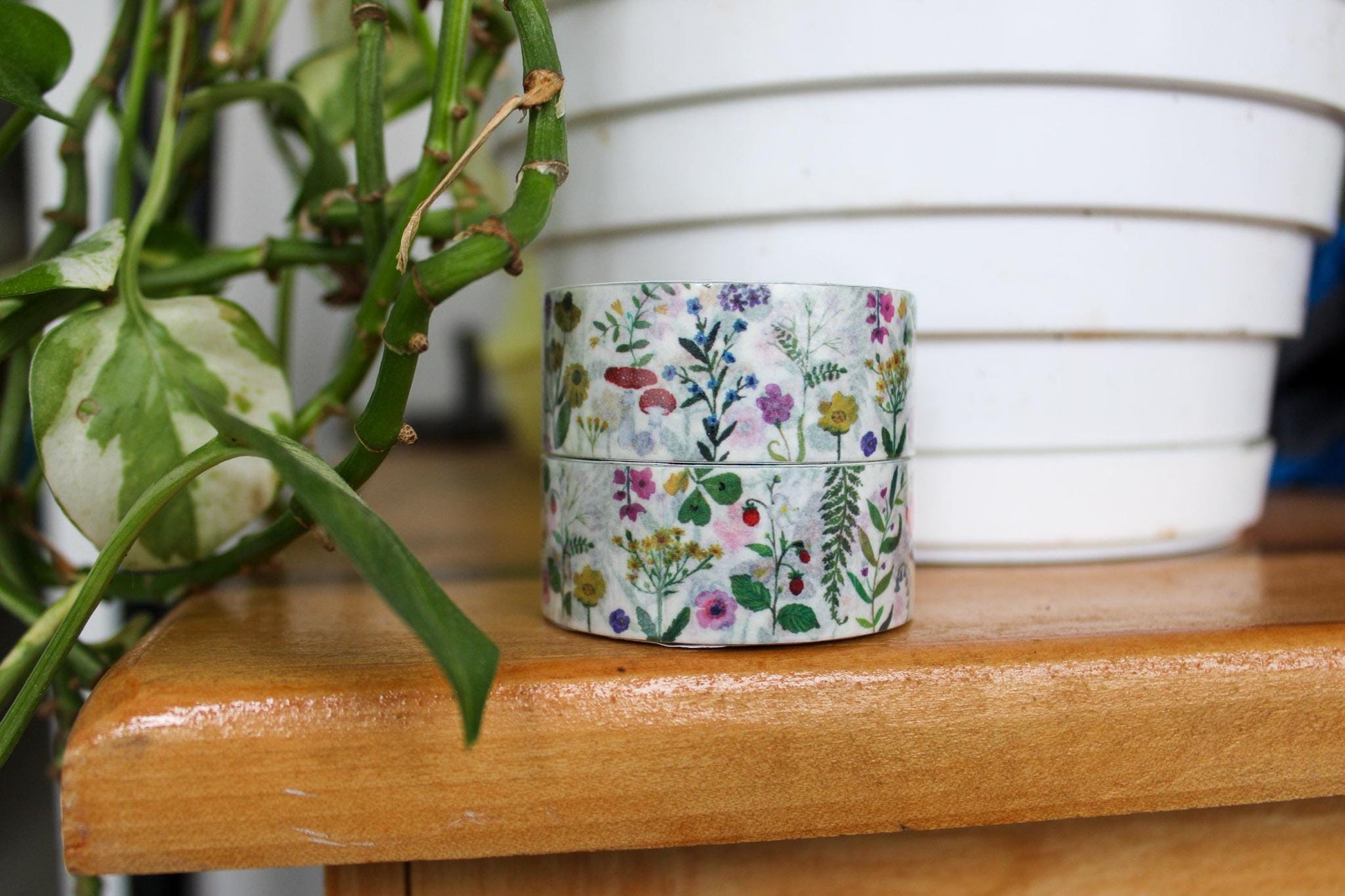 Stack of floral-patterned tape on a wooden surface with a plant in the background