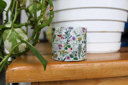 Stack of floral-patterned tape on a wooden surface with a plant in the background