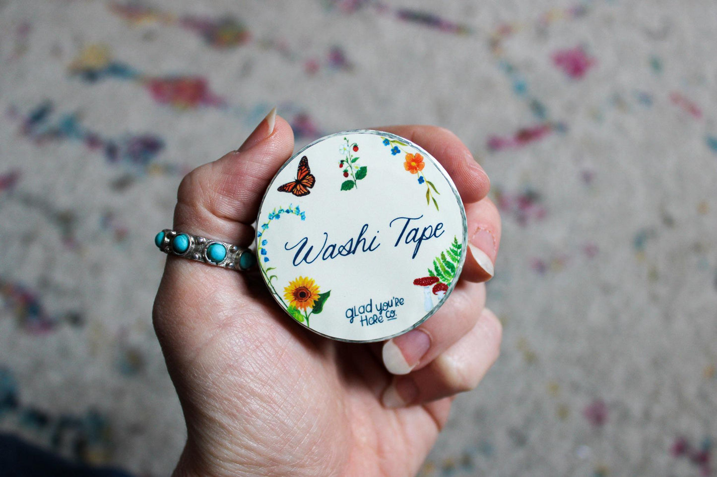 Hand holding a roll of washi tape with decorative design and text.