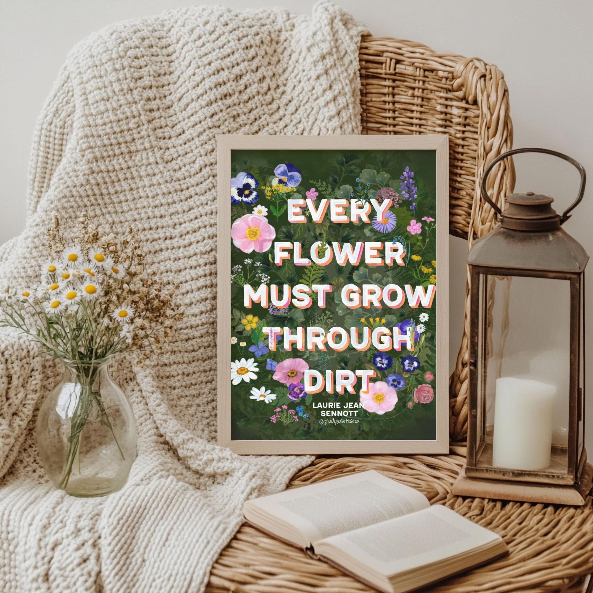 Decorative poster with floral design and text on a wicker surface with candle and flowers.